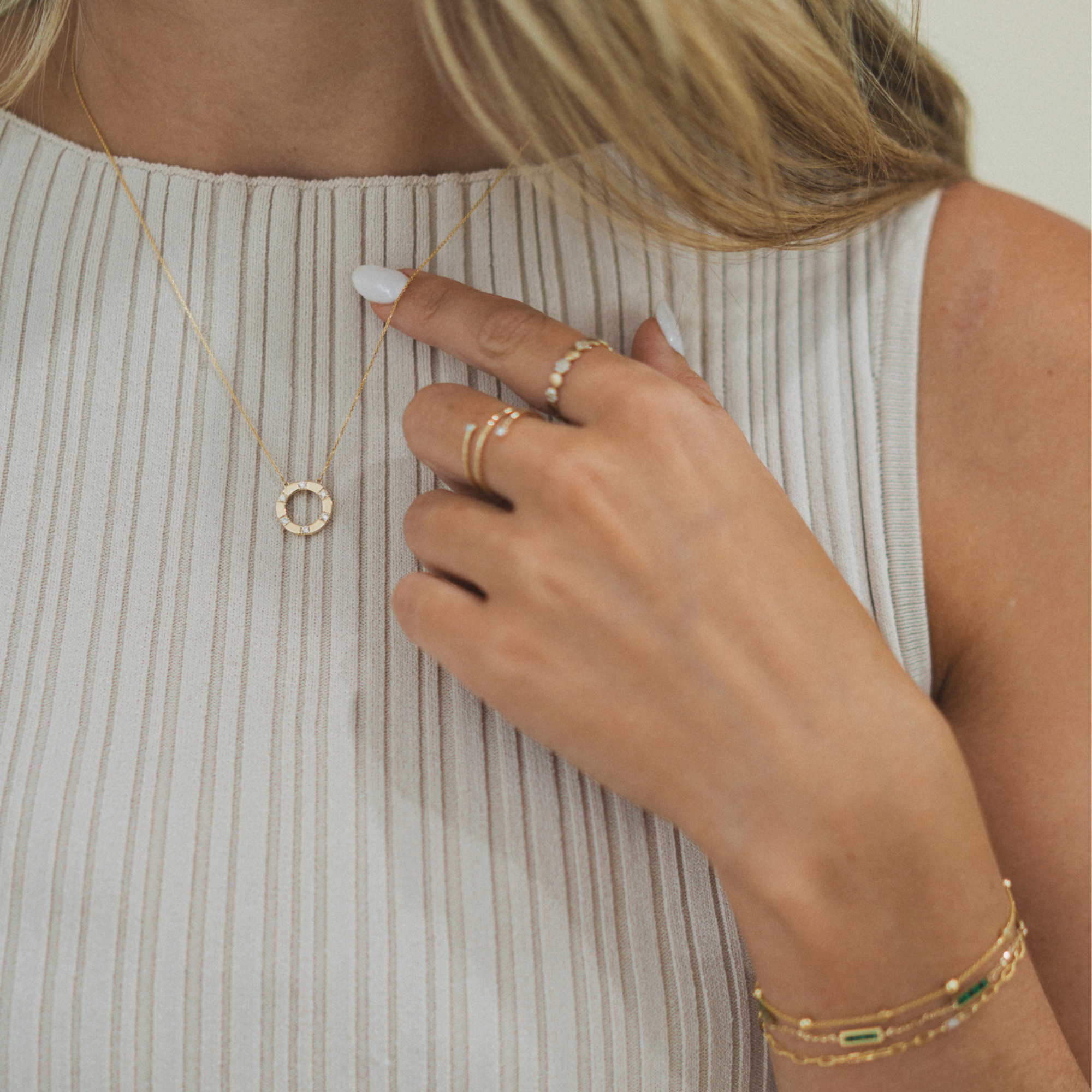 Person touching necklace while wearing bracelets and rings, showcasing elegant gold jewelry.
