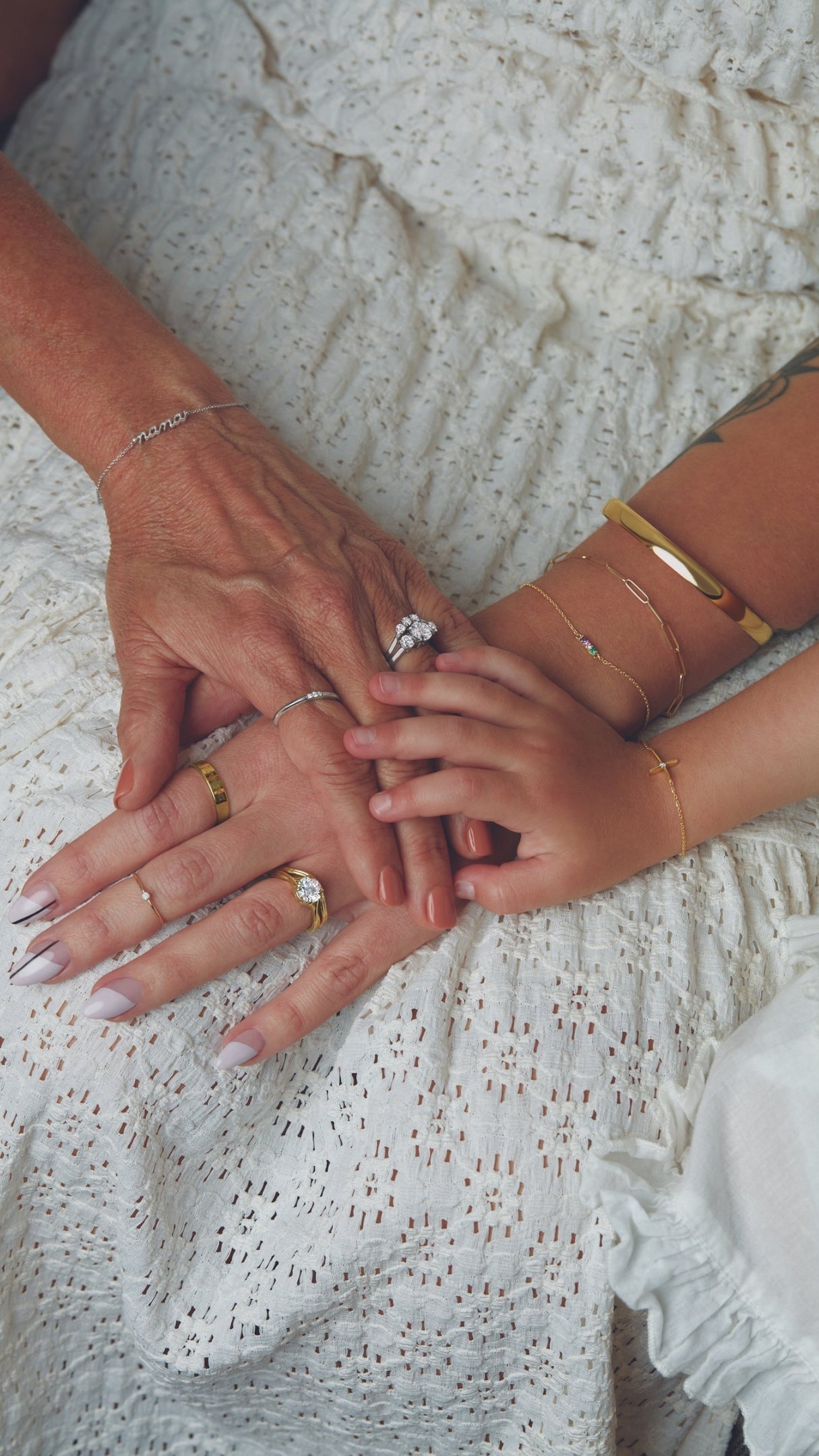 a grandmother, mother, and childs hands layered together with pieces of heirloom jewelry